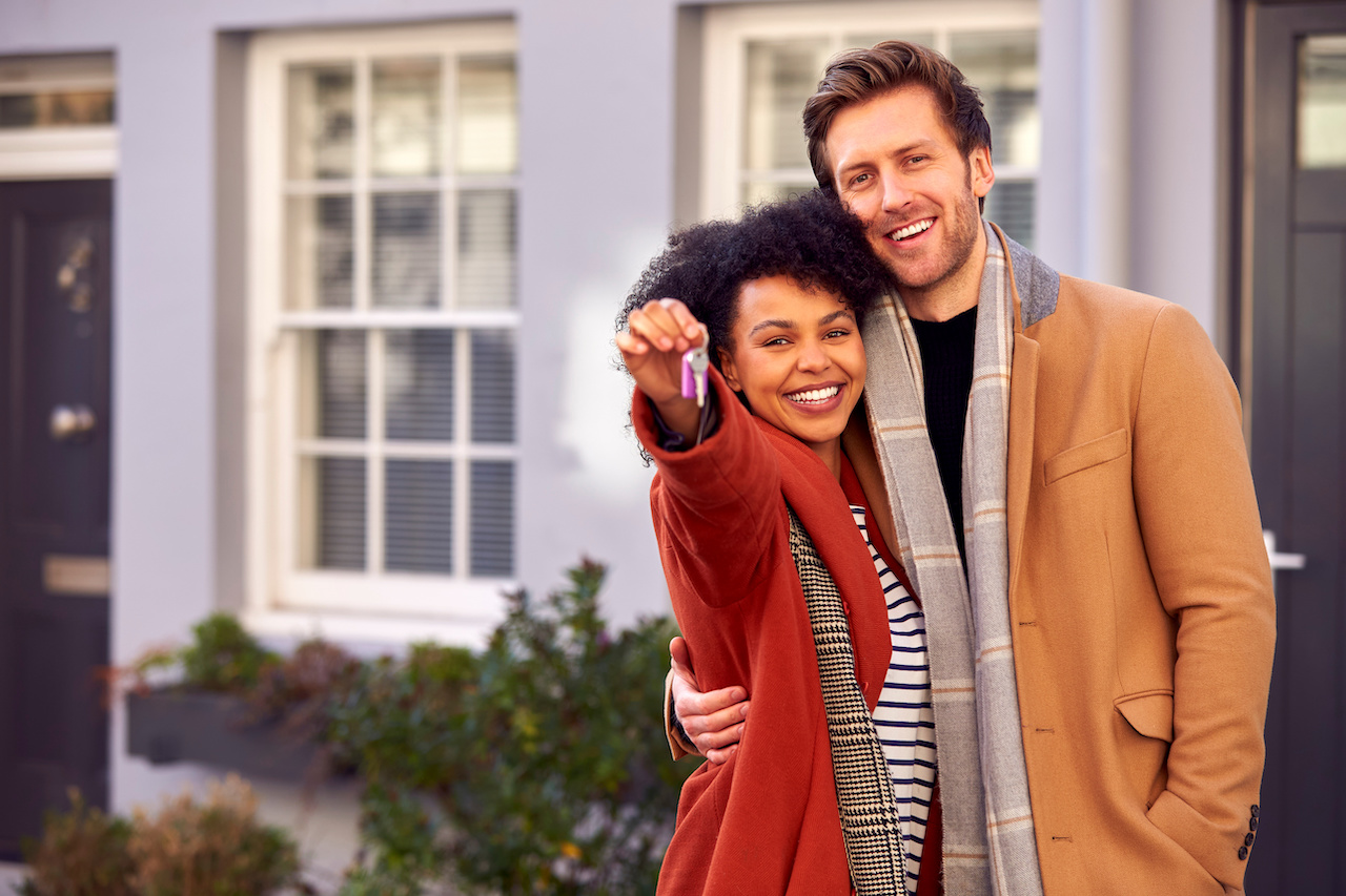 Portrait Of Multi Cultural Couple Outdoors On Moving Day Holding Keys To New Home In Fall Or Winter